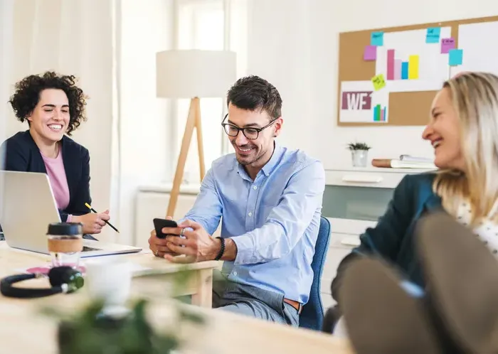 Smiling coworkers in a bright office discuss plans around laptops, illustrating friendly local business support and guidance on City Service Check